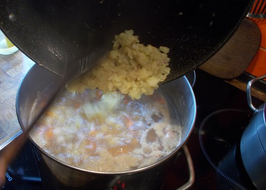 Nach dem Mehlieren die Speck/Zwiebel/Knoblauch-Mischung mit der Kartoffel-Gemüse-Mischung in die Suppe geben und einrühren.