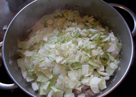 Dann das geschnittene Kraut beigeben und gut vermischen. Das Kraut lässt Wasser, also ist keine zusätzliche Flüssigkeit nötig. Deckel drauf und bei mittlerer Hitze dünsten lassen, ab und zu umrühren, bis das Kraut weich ist. Das geht relativ flott.